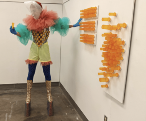 person in colorful costume at artwork made from pill bottles
